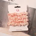 Detailed view of four soft pink satin scrunchies displayed on a white product card - Off White