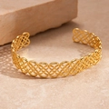 Detalle de un brazalete dorado geométrico calado con textura metálica entrelazada - Dorado