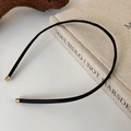 Close-up of slim black leather headband with textured finish and golden metal ends - Bright Black