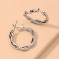 Elegante silberne gedrehte Creolen mit geometrischem Design auf warmem Hintergrund - Silber