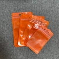Macro view of five stacked orange aluminum foil zip lock bags with hanging holes - Orange (6x10cm)