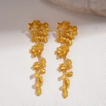 Detailed view of golden leaf and flower drop earrings on a textured stone surface - Gold