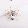 Macro shot of spider brooch with gold metal legs, rhinestones, and large teardrop crystal - White