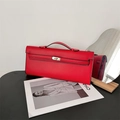 Detail of red leather handbag with metallic clasp closure and top handle on black surface - Red