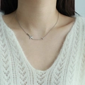 Collana minimale a croce argentata con strass indossata da una donna in maglia bianca - Collana a Croce / Color Acciaio
