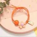 Orange bow hair tie featuring a floral charm and gold metal plate on a pink display base - Orange Custom ID Flower (Alt)