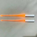Close-up of bright orange LED glowing chopsticks with white handles on gray background - Orange