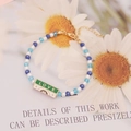Macro detail of handmade beaded bracelet with blue crystals and green LOVE enamel plaque - Green LOVE Style