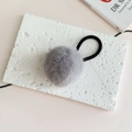 Close-up of a soft grey faux fur pompom hair tie on a minimalist textured stone surface - Gray