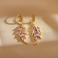 Detailed macro view of gold leaf drop earrings with purple marquise cut stones on fabric - Pink
