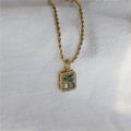 Detalle de collar de cadena dorada con colgante de gema verde rectangular y circonitas - Collar / Zircón Verde