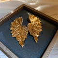 Macro view of gold leaf-shaped earrings with intricate vein textures in a jewelry box - Gold Leaf Style (Silver Needle)