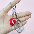 Detail showing a mini red felt tennis ball and silver racket keychain held in hand - 2cm Ball / Red
