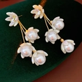 Makro-Detail von goldenen Blumen-Ohrringen mit weißen Perlen auf grünem Samt - Gold