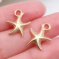 Two small golden starfish charms for DIY jewelry held on a finger to show mini size - Sea Star Pendant 13x15.5mm