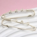 Detail of 6cm beige painted safety pins with three loops on a pink and white grid base - Off-white