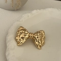 Close-up of golden bow-shaped metal hair tie with hammered texture on a ceramic plate - Gold-Bowknot