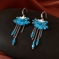 Détail de boucles d'oreilles pompons en cristal bleu avec motif pétale sur socle sombre - Crochet Argent Cristal Bleu