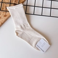 Close-up of cream cotton crew socks with ribbed knit texture and brand logo tag - One Size / Beige
