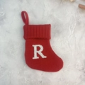 Red knitted Christmas stocking with white embroidered letter R on a grey background - Letter R