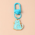 Close-up of light blue enamel cat keychain with gold trim on soft peach background - Blue Full Body Cat