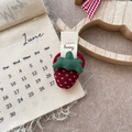 Detail view of a red fabric strawberry hair scrunchie with green leaves on a table - Strawberry Hair Tie