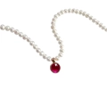 Detailed close-up of a white pearl necklace with a circular red gemstone pendant in gold - July Ruby