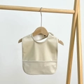 Close-up of beige waterproof baby bib with food catcher pocket on wooden hanger - Beige