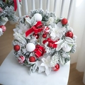 Artificial Christmas wreath with flocked pine, red bow and ornaments on a white chair - Red and White Wreath
