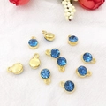 Golden constellation charms with blue faceted rhinestones on textured white fabric background - Gold March - Blue