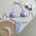Detail of purple metallic bikini featuring elegant pearl and gold ring accents on woven mat - White