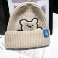 Beige knit beanie with bear embroidery and blue classic label on soft background - One Size / Beige (With Bear Embroidery)