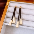 Primer plano de pendientes de borla con cordón de cuero oscuro y piezas metálicas en oro mate - Estilo de Pendent de Oro Mate / Dorado
