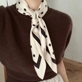 Gros plan d'un foulard en soie beige à pois noirs et bordure porté autour du cou - Pois Blancs