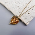 Close-up of heart-shaped amber pendant with gold foil texture and golden chain - Gold-Amber