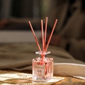 Dettaglio di un diffusore in vetro con olio profumato rosa su un tappetino di bambù - Rosa