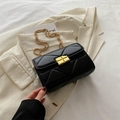 Quilted black crossbody bag with gold chain strap and square lock on beige blazer - Black