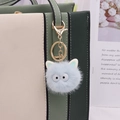 Detalle de un llavero de pompón azul claro de piel sintética colgado en un bolso chic - Cierre de Cadena Dorada / Azul claro