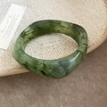 Detail van een groene hars armband met marmeren textuur op een beige geweven dienblad - Donkergroen
