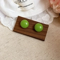 Detail view of grass green bean stud earrings displayed on a dark wood board - Green