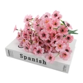 Artificial pink silk flower bouquet with purple textures and green stems on white book - Pink