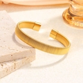 Elegante gouden geweven mesh open manchetarmband gepresenteerd op minimalistische steen - Goud