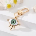 Porte-clés œil maléfique doré avec iris vert et strass sur fond en marbre blanc élégant - Oeil Vert Strass