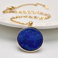 Golden necklace with circular dark blue lapis lazuli stone pendant on white ceramic plate - Round