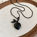 Detail of a polished black heart stone pendant on a woven cord necklace on a wood tray - Black