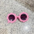 Pink flower-shaped kids sunglasses with dark UV lenses on a grey stone surface - Glossy Candy Pink