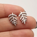 Minimalist silver leaf stud earrings in matte stainless steel shown on a fingertip - Leaf / Steel
