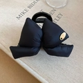 Detail of black puffy bow hair claw clip with gold metal tag on a minimal book background - Black