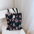 Dettaglio della borsa tote in tela floreale con tulipani rosa su una sedia bianca - Nero con fiori rossi