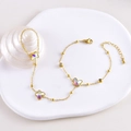Detailed close-up of gold butterfly hand chain with colorful charms on white plate - Three Butterflies